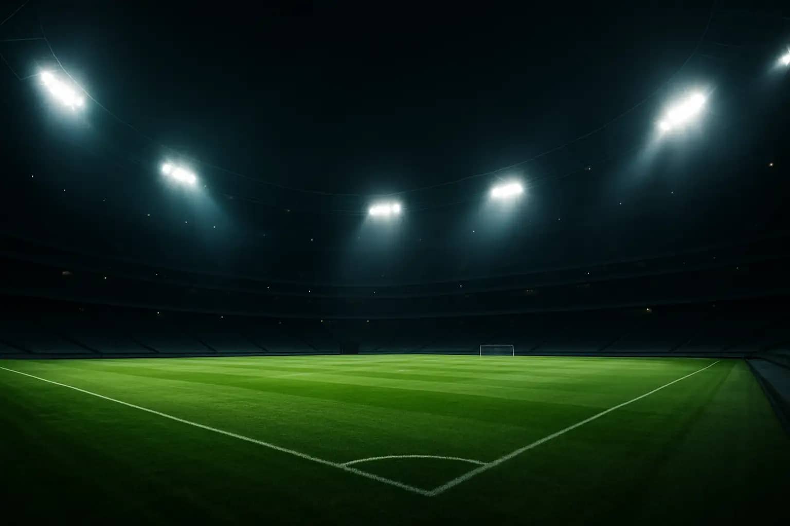 A football stadium at night with floodlights illuminating an empty green pitch